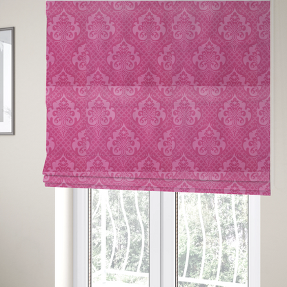 The fabric used to create these Roman blinds has a design that features large, ornate floral medallions and scrolling acanthus leaves in a lighter pink shade, set against a saturated magenta-rose background. A fine diagonal lattice grid fills the background between the motifs, and the material shows a clear woven texture that provides visual depth to the traditional design.