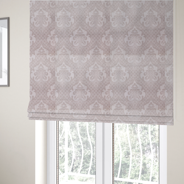 The fabric used to create these Roman blinds has a baby pink and cream damask pattern on a textured fabric. The design features large, ornate floral medallions with stylized acanthus leaf scrolls, arranged in a structured, repeating grid.