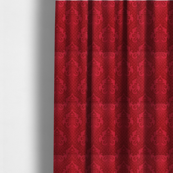 The fabric used to create these made-to-measure curtains has a design that features large, ornate floral medallions and scrolling acanthus leaves in a slightly lighter shade of red, creating a tonal, high-contrast effect. A fine diagonal lattice grid fills the background between the motifs, and the material shows a clear woven texture that adds depth and a traditional feel to the design.