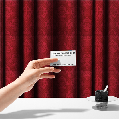 The fabric used to create these made-to-measure curtains has a design that features large, ornate floral medallions and scrolling acanthus leaves in a slightly lighter shade of red, creating a tonal, high-contrast effect. A fine diagonal lattice grid fills the background between the motifs, and the material shows a clear woven texture that adds depth and a traditional feel to the design.