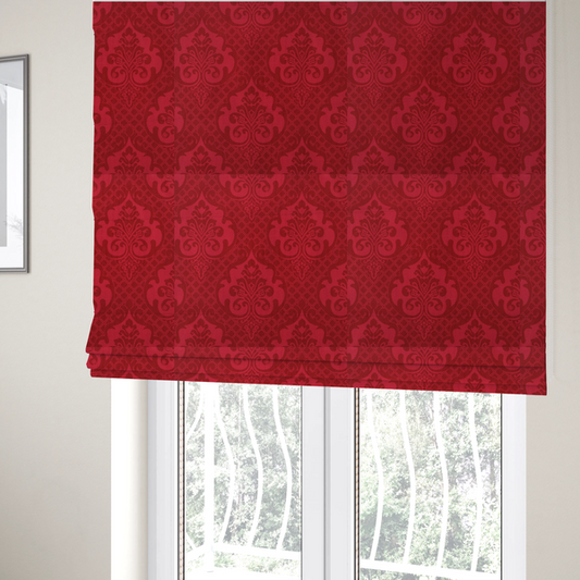 The fabric used to create these Roman blinds has a design that features large, ornate floral medallions and scrolling acanthus leaves in a slightly lighter shade of red, creating a tonal, high-contrast effect. A fine diagonal lattice grid fills the background between the motifs, and the material shows a clear woven texture that adds depth and a traditional feel to the design.