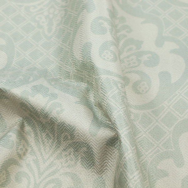 The design showcases large, ornate floral medallions and scrolling acanthus leaves in a light silver shade, set against a slightly darker grey-white background. A fine diagonal lattice grid creates a diamond pattern in the negative space between the motifs, and the material displays a clear woven texture that adds a sophisticated, metallic-like shimmer to the pattern.