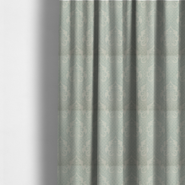 The fabric used to create these made-to-measure curtains has a design that showcases large, ornate floral medallions and scrolling acanthus leaves in a light silver shade, set against a slightly darker grey-white background. A fine diagonal lattice grid creates a diamond pattern in the negative space between the motifs, and the material displays a clear woven texture that adds a sophisticated, metallic-like shimmer to the pattern.