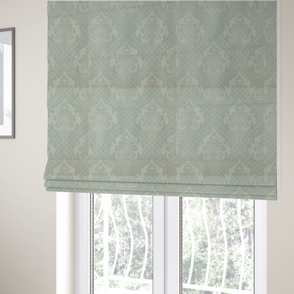 The fabric used to create these Roman blinds has a design that showcases large, ornate floral medallions and scrolling acanthus leaves in a light silver shade, set against a slightly darker grey-white background. A fine diagonal lattice grid creates a diamond pattern in the negative space between the motifs, and the material displays a clear woven texture that adds a sophisticated, metallic-like shimmer to the pattern.