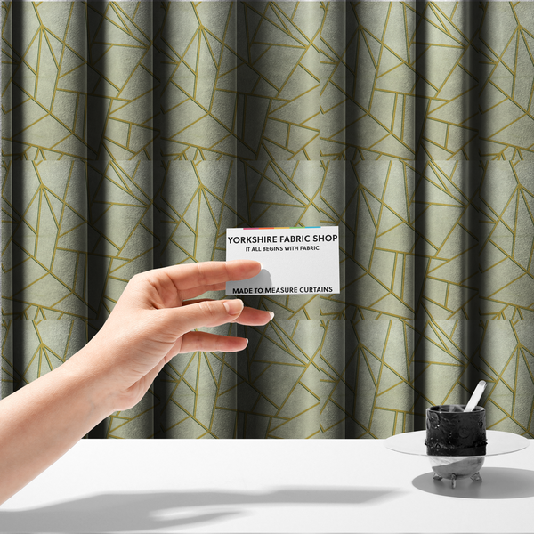 The fabric used to create these made-to-measure curtains, features a geometric, fractured glass pattern. The design consists of irregular, sharp-angled polygons in a pale sage green or muted seafoam hue. These shapes are separated by thick, shimmering gold metallic lines that appear slightly recessed or embossed, creating a high-contrast, mosaic-like effect.