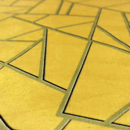 A close-up of a luxurious mustard yellow fabric featuring a bold geometric, fractured pattern. The design is composed of sharp, irregular polygons separated by embossed tone-on-tone lines in a slightly darker, olive-tinted gold.