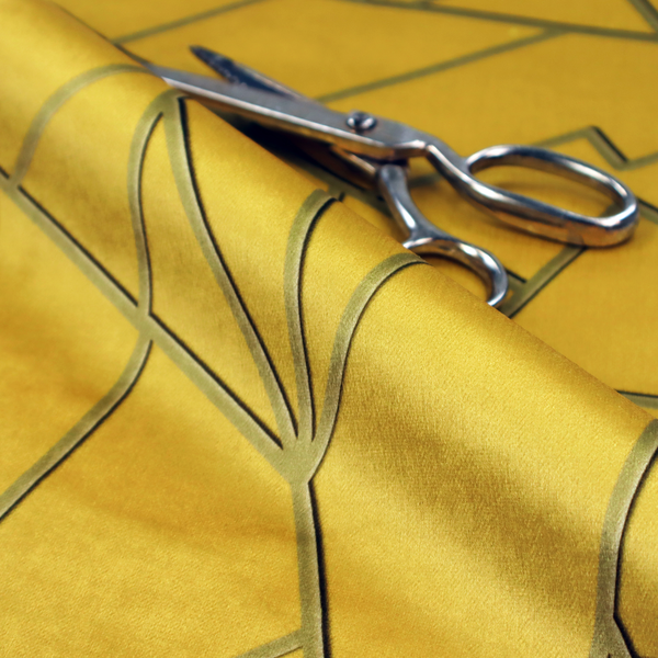 A close-up of a luxurious mustard yellow fabric featuring a bold geometric, fractured pattern. The design is composed of sharp, irregular polygons separated by embossed tone-on-tone lines in a slightly darker, olive-tinted gold.