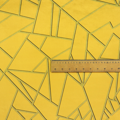 A close-up of a luxurious mustard yellow fabric featuring a bold geometric, fractured pattern. The design is composed of sharp, irregular polygons separated by embossed tone-on-tone lines in a slightly darker, olive-tinted gold.