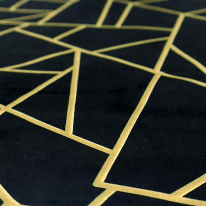 A close-up of a high-contrast black and gold fabric featuring a fractured, geometric mosaic design. The deep, matte black background is intersected by a network of sharp, metallic gold lines that form irregular, angular polygons. The pattern resembles a web of shimmering gold veins or a stylized shattered-glass effect, giving the textile a luxurious, Art Deco-inspired aesthetic.