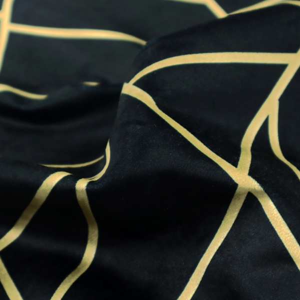 A close-up of a high-contrast black and gold fabric featuring a fractured, geometric mosaic design. The deep, matte black background is intersected by a network of sharp, metallic gold lines that form irregular, angular polygons. The pattern resembles a web of shimmering gold veins or a stylized shattered-glass effect, giving the textile a luxurious, Art Deco-inspired aesthetic.