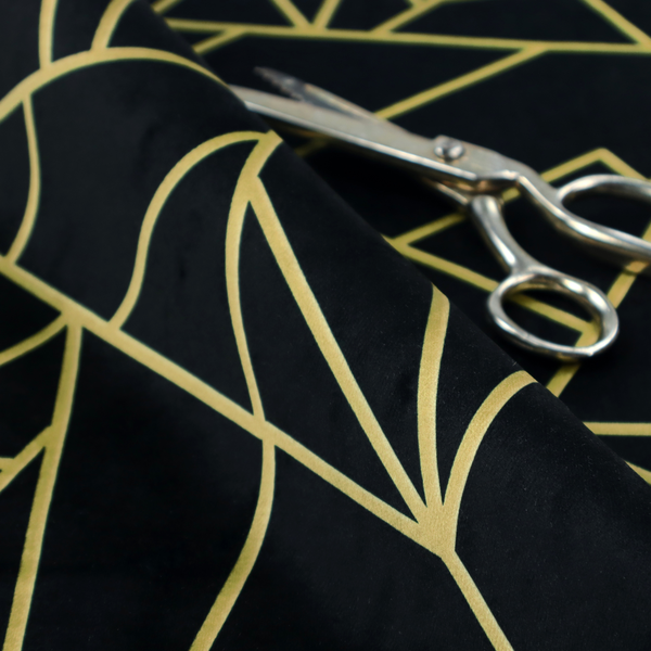 A close-up of a high-contrast black and gold fabric featuring a fractured, geometric mosaic design. The deep, matte black background is intersected by a network of sharp, metallic gold lines that form irregular, angular polygons. The pattern resembles a web of shimmering gold veins or a stylized shattered-glass effect, giving the textile a luxurious, Art Deco-inspired aesthetic.
