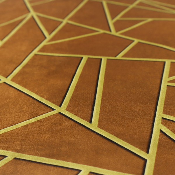 A close-up of a luxurious brown or rust-coloured fabric featuring a fractured, geometric mosaic pattern. The warm, matte background is divided by a network of recessed gold metallic lines that form sharp, irregular polygons. This "cracked ice" or shattered-glass effect creates a bold, architectural look, blending the deep, earthy tones of the textile with shimmering, Art Deco-inspired accents.