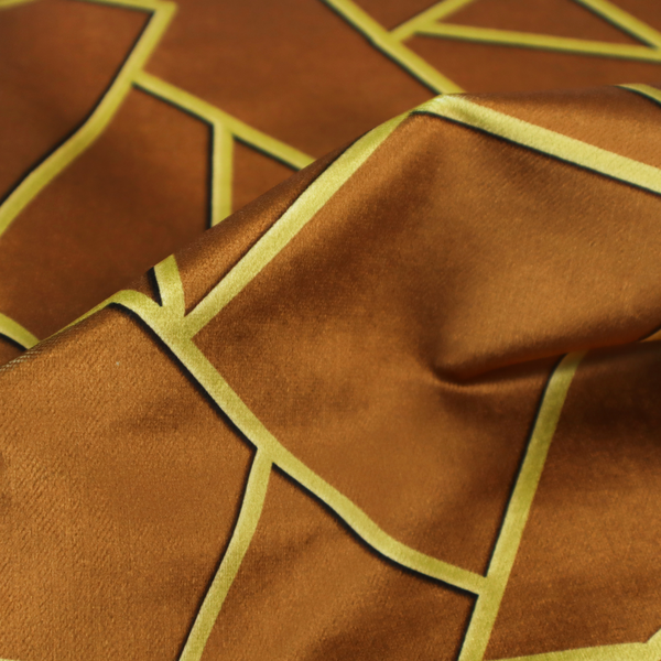 A close-up of a luxurious brown or rust-coloured fabric featuring a fractured, geometric mosaic pattern. The warm, matte background is divided by a network of recessed gold metallic lines that form sharp, irregular polygons. This "cracked ice" or shattered-glass effect creates a bold, architectural look, blending the deep, earthy tones of the textile with shimmering, Art Deco-inspired accents.