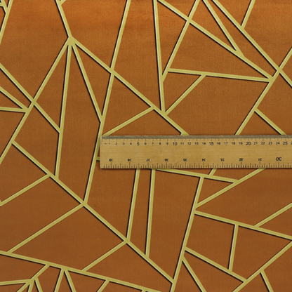 A close-up of a luxurious brown or rust-coloured fabric featuring a fractured, geometric mosaic pattern. The warm, matte background is divided by a network of recessed gold metallic lines that form sharp, irregular polygons. This "cracked ice" or shattered-glass effect creates a bold, architectural look, blending the deep, earthy tones of the textile with shimmering, Art Deco-inspired accents.