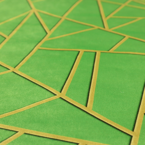 A close-up of a vibrant bright green fabric featuring a fractured, geometric mosaic pattern. The lively, matte background is segmented by a network of recessed metallic gold lines that form sharp, irregular polygons. This "cracked ice" or shattered-glass effect creates a bold, modern look, combining a lush, verdant base with shimmering, Art Deco-inspired accents.