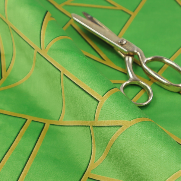 A close-up of a vibrant bright green fabric featuring a fractured, geometric mosaic pattern. The lively, matte background is segmented by a network of recessed metallic gold lines that form sharp, irregular polygons. This "cracked ice" or shattered-glass effect creates a bold, modern look, combining a lush, verdant base with shimmering, Art Deco-inspired accents.