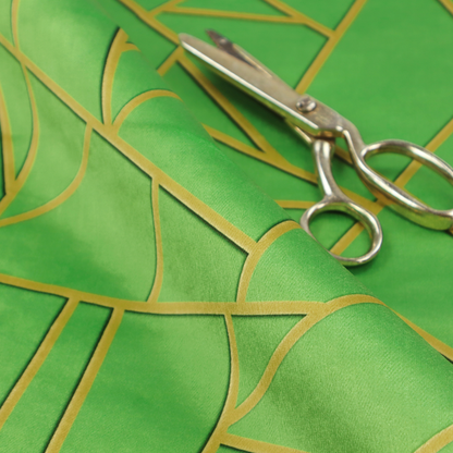 A close-up of a vibrant bright green fabric featuring a fractured, geometric mosaic pattern. The lively, matte background is segmented by a network of recessed metallic gold lines that form sharp, irregular polygons. This "cracked ice" or shattered-glass effect creates a bold, modern look, combining a lush, verdant base with shimmering, Art Deco-inspired accents.