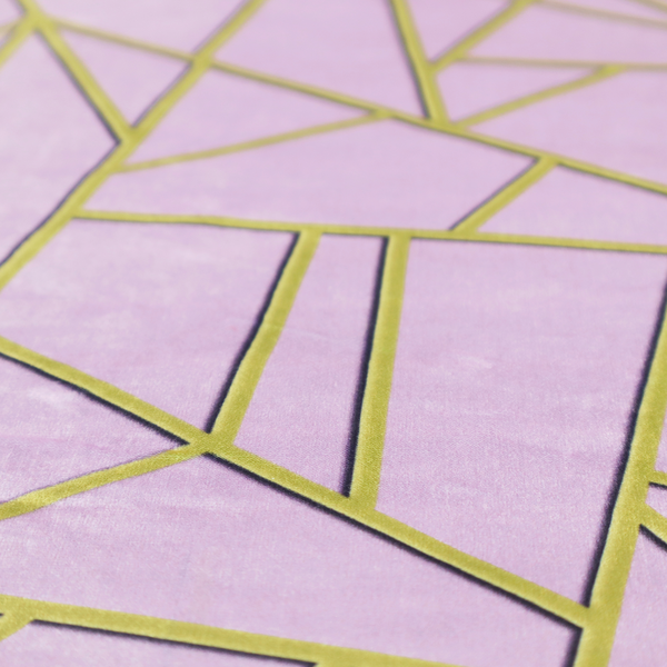A close-up of a luxurious lavender or lilac fabric featuring a fractured, geometric mosaic pattern. The soft, matte background is segmented by a network of recessed metallic gold lines that form sharp, irregular polygons. This "shattered-glass" effect creates a sophisticated visual contrast, blending the delicate, feminine tones of the textile with shimmering, Art Deco-inspired gold accents for a clean and contemporary look.