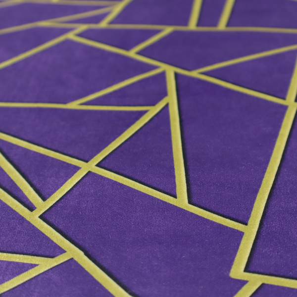 A close-up of a luxurious deep purple or violet fabric featuring a fractured, geometric mosaic pattern. The dark, matte background is segmented by a network of recessed metallic gold lines that form sharp, irregular polygons. This "shattered-glass" effect creates a dramatic visual contrast, blending the rich, royal tones of the textile with shimmering, Art Deco-inspired gold accents for a bold and sophisticated look.