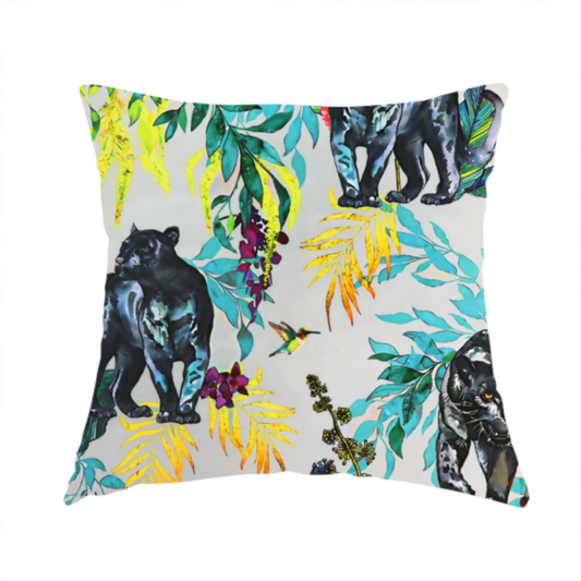 The fabric used to create this handmade cushion is a vibrant tropical fabric print featuring sleek black panthers prowling among exotic flora. The design includes colourful botanical elements like oversized teal and lime green leaves, magenta flowers, and yellow ferns. Small details like a soaring owl and a hummingbird are scattered throughout on a pale grey background.