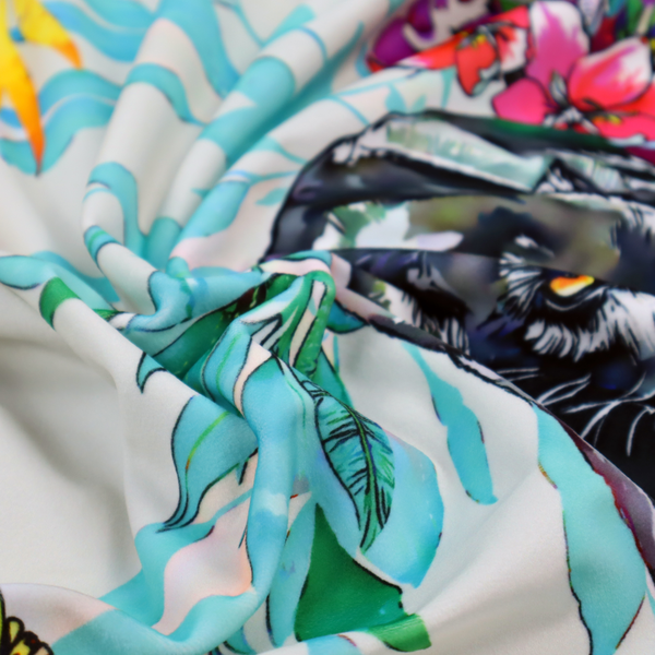 A vibrant tropical fabric print featuring sleek black panthers prowling among exotic flora. The design includes colourful botanical elements like oversized teal and lime green leaves, magenta flowers, and yellow ferns. Small details like a soaring owl and a hummingbird are scattered throughout on a pale grey background.