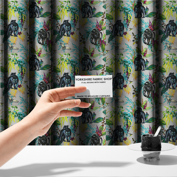 The fabric used to create these made-to-measure curtains is a vibrant tropical fabric print featuring sleek black panthers prowling among exotic flora. The design includes colourful botanical elements like oversized teal and lime green leaves, magenta flowers, and yellow ferns. Small details like a soaring owl and a hummingbird are scattered throughout on a pale grey background.
