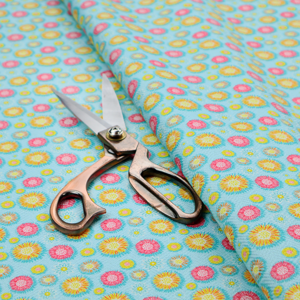 Light blue fabric featuring an all-over repeating pattern of vibrant pink and gold floral motifs interspersed with small yellow dotted accents.
