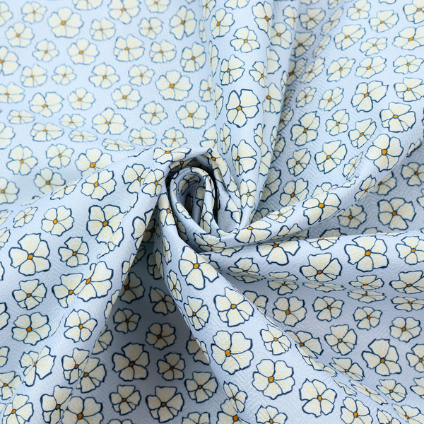 A light blue fabric featuring a dense, repeating pattern of small white flowers with yellow centres and dark outlines.