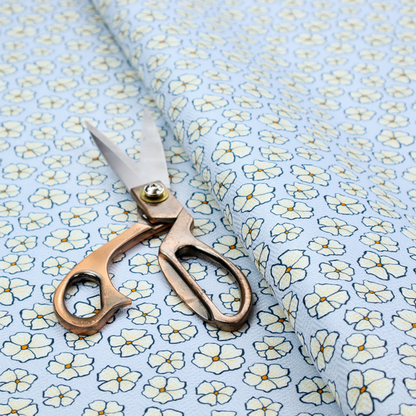 A light blue fabric featuring a dense, repeating pattern of small white flowers with yellow centres and dark outlines.