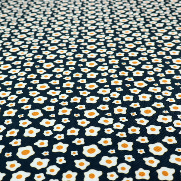 A dark navy blue fabric featuring a dense, repeating pattern of small fried egg motifs with white whites and yellow yolks.