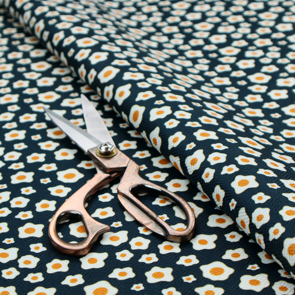A dark navy blue fabric featuring a dense, repeating pattern of small fried egg motifs with white whites and yellow yolks.