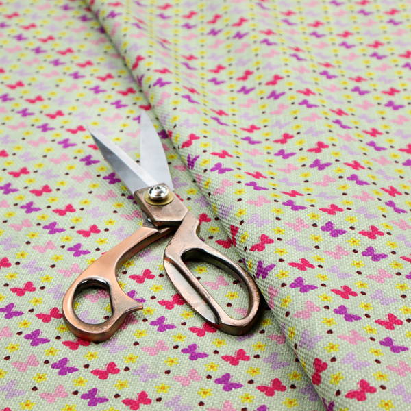A light green fabric featuring a dense, repeating pattern of small multi-coloured butterflies in pink, magenta, and purple, interspersed with tiny yellow flowers and dots.