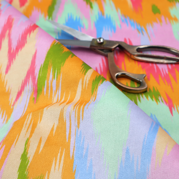 This fabric features a vibrant, multi-coloured ikat-style pattern with a soft, blurred aesthetic.
