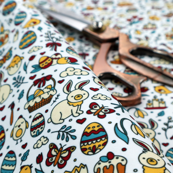 This fabric features a whimsical, hand-drawn Easter doodle pattern set against a clean, pale blue-grey background. The design is a dense, "scatter" style print using a primary colour palette of deep red, mustard yellow, and teal blue.