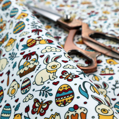 This fabric features a whimsical, hand-drawn Easter doodle pattern set against a clean, pale blue-grey background. The design is a dense, "scatter" style print using a primary colour palette of deep red, mustard yellow, and teal blue.