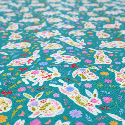 This fabric features a vibrant, folk-art inspired Easter pattern set against a rich teal-green background. The design is characterized by its high-contrast colour palette and intricate floral silhouettes.