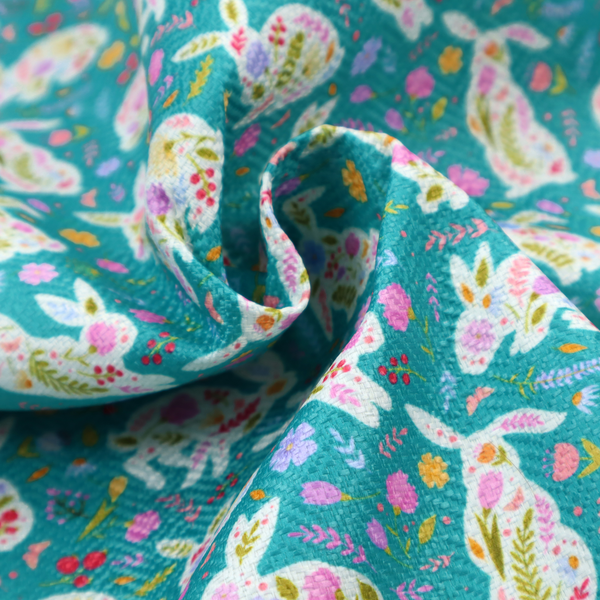 This fabric features a vibrant, folk-art inspired Easter pattern set against a rich teal-green background. The design is characterized by its high-contrast colour palette and intricate floral silhouettes.