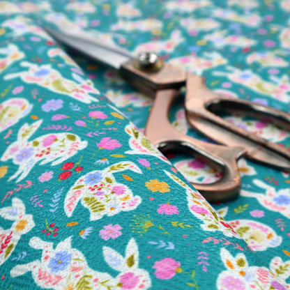 This fabric features a vibrant, folk-art inspired Easter pattern set against a rich teal-green background. The design is characterized by its high-contrast colour palette and intricate floral silhouettes.