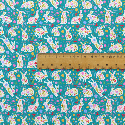 This fabric features a vibrant, folk-art inspired Easter pattern set against a rich teal-green background. The design is characterized by its high-contrast colour palette and intricate floral silhouettes.