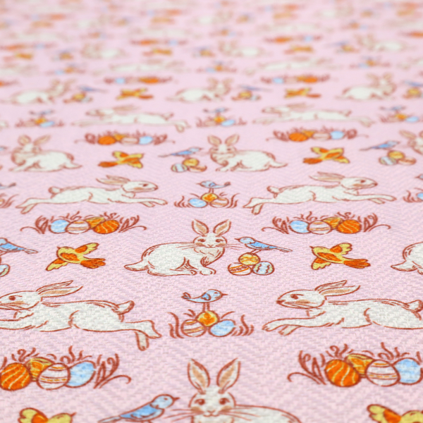 This fabric features a vintage-style Easter meadow pattern on a soft, blush-pink background. The design is reminiscent of classic children’s book illustrations, using fine, orange-brown linework and a muted pastel palette.