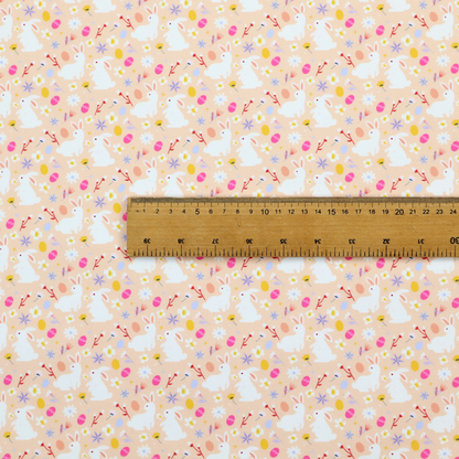 This fabric features a delicate, dainty Easter meadow pattern on a soft, peachy-beige background. The design is airy and feminine, characterized by small-scale illustrations and a palette of pastel and vibrant spring colours.