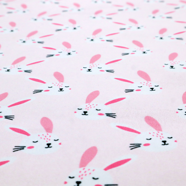 This fabric features a modern, minimalist bunny pattern set against a soft, pale pink background. The design is clean and contemporary, focusing on a repeating motif of stylized rabbit faces.