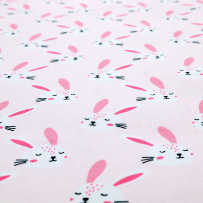 This fabric features a modern, minimalist bunny pattern set against a soft, pale pink background. The design is clean and contemporary, focusing on a repeating motif of stylized rabbit faces.