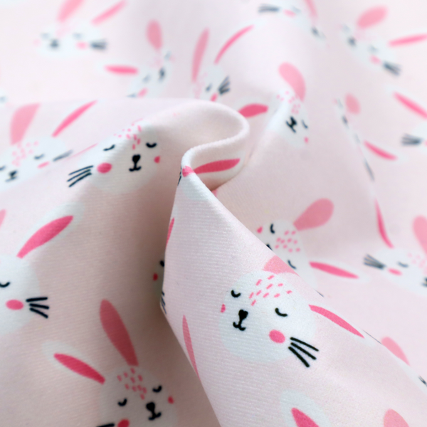 This fabric features a modern, minimalist bunny pattern set against a soft, pale pink background. The design is clean and contemporary, focusing on a repeating motif of stylized rabbit faces.