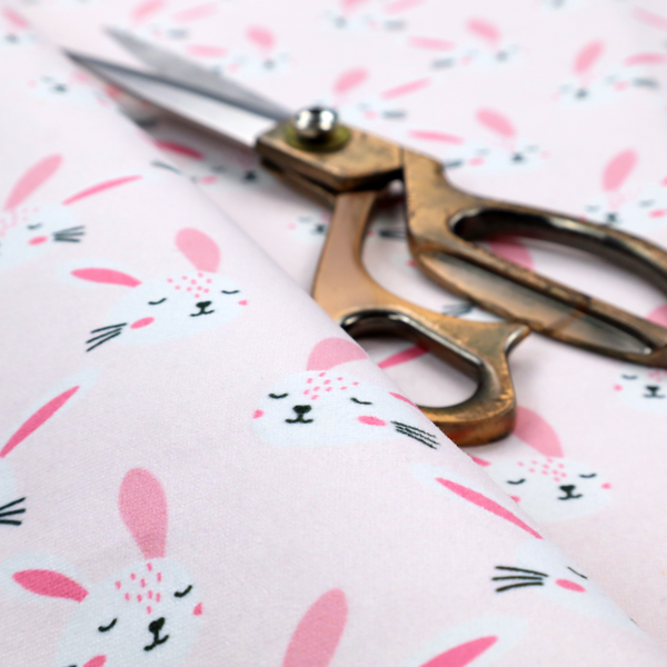 This fabric features a modern, minimalist bunny pattern set against a soft, pale pink background. The design is clean and contemporary, focusing on a repeating motif of stylized rabbit faces.