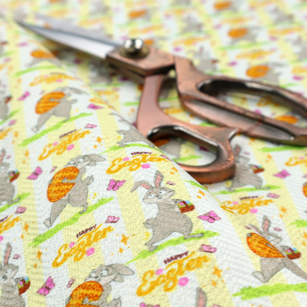 This fabric features a cheery and active Easter bunny pattern set against a vertical striped background of pale yellow and white. The design has a classic animated feel, full of personality and holiday spirit.