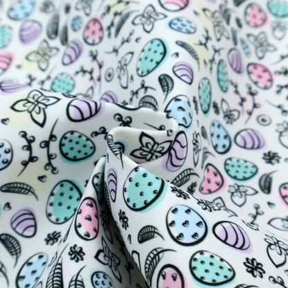 This fabric features an artistic, hand-illustrated Easter egg pattern on a cool, pale blue background. The design has a sketchbook or "doodle" quality, with expressive black ink outlines and soft watercolour-style colour accents.