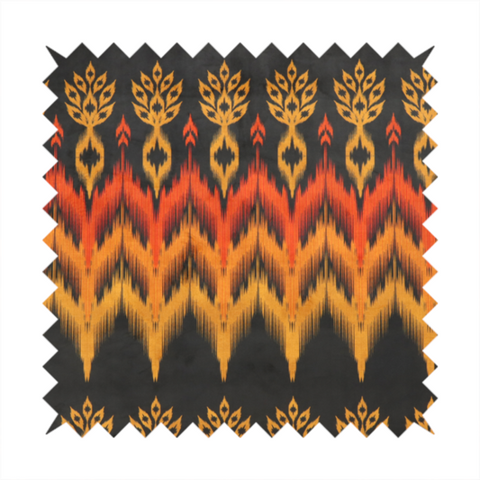 A bold ethnic-inspired fabric featuring a horizontal Ikat border design. The pattern showcases jagged, flame-like chevron stripes in vibrant orange and saffron yellow, flanked by rows of stylized tribal leaf motifs on a dark charcoal-grey background.
