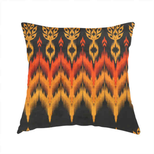 The fabric used to create these handmade cushions is a bold ethnic-inspired fabric featuring a horizontal Ikat border design. The pattern showcases jagged, flame-like chevron stripes in vibrant orange and saffron yellow, flanked by rows of stylized tribal leaf motifs on a dark charcoal-grey background.