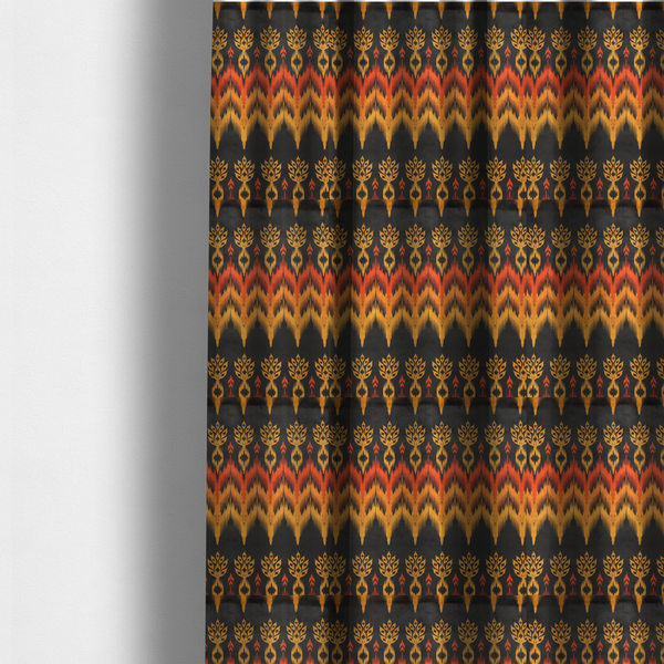 The fabric used to create these made-to-measure curtains is a bold ethnic-inspired fabric featuring a horizontal Ikat border design. The pattern showcases jagged, flame-like chevron stripes in vibrant orange and saffron yellow, flanked by rows of stylized tribal leaf motifs on a dark charcoal-grey background.